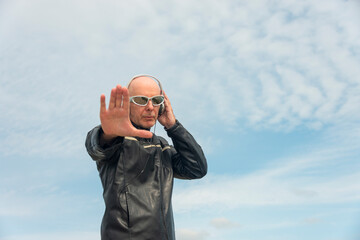 Fototapeta premium Attractive bald man with sunglasses and headphones. Outdoors with blue sky background