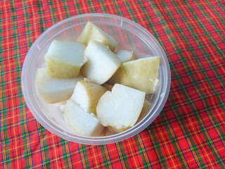 Lontong, Indonesian rice cakes cut into bite-sized pieces, neatly arranged inside a transparent plastic bowl, placed on a plaid red and green tablecloth, creating a vibrant presentation