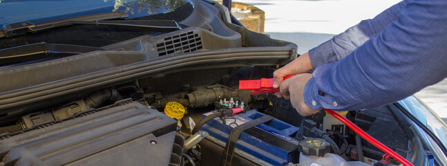 Image of a man's hands holding battery cables to jump start a broken down car
