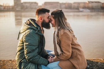 Happy couple holding hands while enjoy spending time together outdoor. Man is kissing his woman in nose.