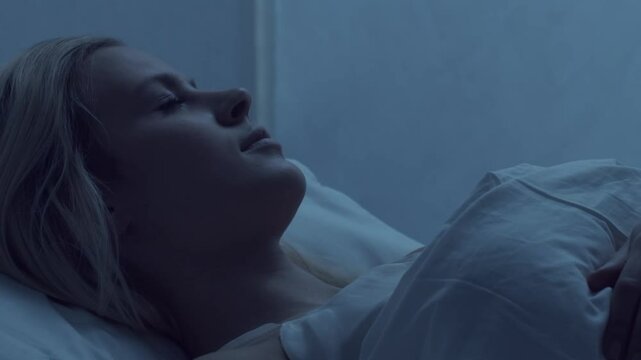 Young woman lying in the bed at night and having insomnia disease. Beautiful blond sleeping girl. Twilight in the bedroom, moonlight from the window. Sleeplessness, health and rest concept.