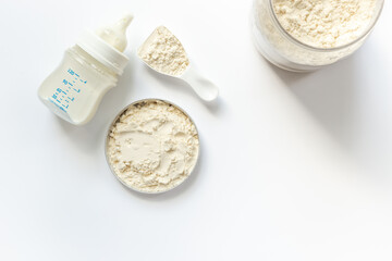 Jar of powdered milk for baby food with bottle of milk and spoon, top view