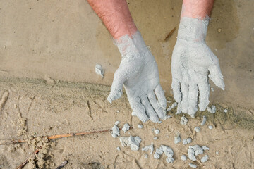 Hands palms up. Blue clay on the man's hands. Mud baths with clay. A layer of clay is applied to the man's hands. Sand and water background.