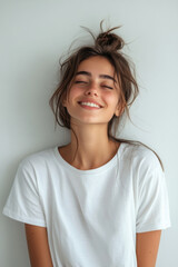 Happy Woman,  A cheerful woman wearing a loose white T-shirt poses against a plain white wall, expressing joy and positivity