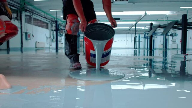 Epoxy floor Construction worker carefully pours epoxy resin to create a smooth and durable floor in a modern industrial facility