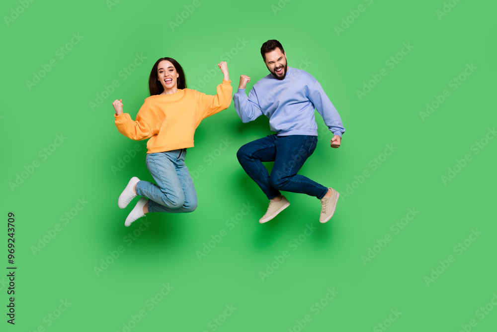 Sticker Photo of cheerful attractive crazy couple wear trendy clothes jump up hand fist yes isolated on green color background