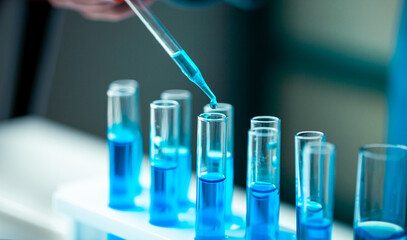 A person is pouring blue liquid into a row of test tubes