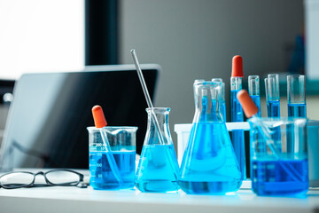 A table with a laptop, a few beakers and test tubes, and a blue liquid. The table is set up for a science experiment