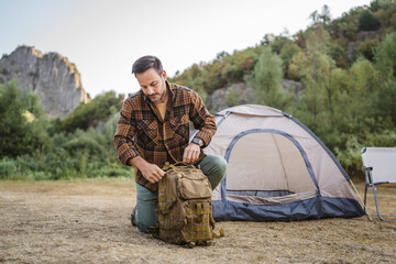 Adult man kneel and pack his backpack ready for going home after camp