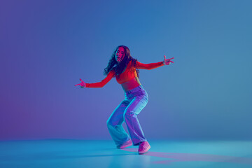 Hip hop training session in full motion, female dancer performing with passion against gradient blue background in neon light. Concept of freestyle dance, modernity, urban culture, youth