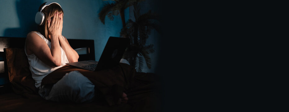 Woman watching a scary horror movie on laptop lying on bed late at night, she is frightened covering face