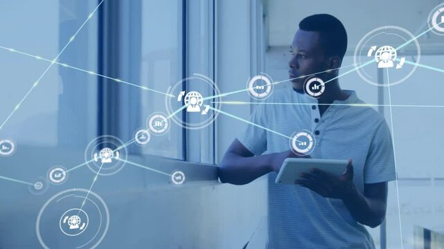 Animation of network of connections with icons over african american businessman using tablet