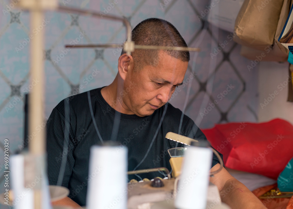 Wall mural candid shot of a middle aged asian tailor busily working inside his modest shop.