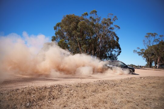 A rally car kicks up dust on a dirt track.