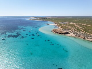 View of a pristine beach with turquoise water and boats near the shore.
