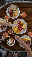 A breakfast table with omelettes, bacon, toast, fresh fruits, and smoothies being enjoyed by people.