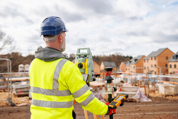 Surveyor in Reflective Gear Using a Total Station on a Construction Site Beneath a Cloudy Sky