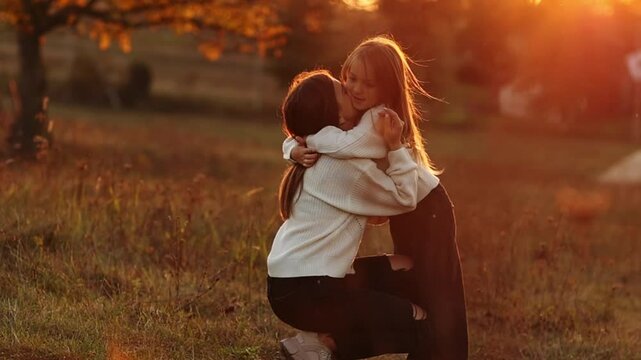 Family day, mother's day. Happy smiling young mom and adorable child daughter soft hugging, kissing and spending time together at autumn on sunset. Idyllic family having fun outdoors on fall holiday