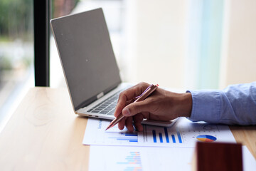 Asian businessman uses pen to analyze graph, real estate market, laptop computer  and borrowed paper in the office