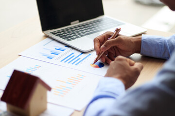 Asian businessman uses pen to analyze graph, real estate market, laptop computer  and borrowed paper in the office