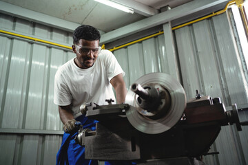 A man is working on a machine in a workshop. He is wearing a white shirt and blue pants