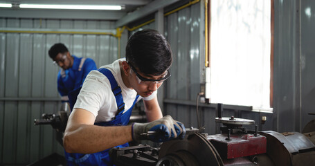 A man in a blue apron is working on a machine. He is wearing safety glasses and gloves