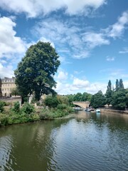 Obraz premium Scenic view of a river with trees and a bridge under a bright blue sky with clouds in Bath, England