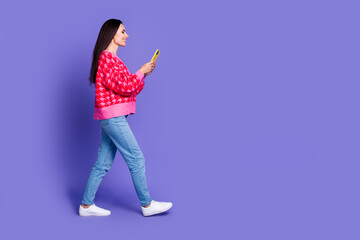 Full length photo of cheerful pretty lady dressed pink cardigan chatting device walking empty space isolated violet color background