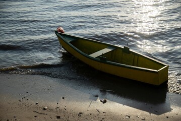 Yellow wooden boat on shore with sunlight reflecting on water