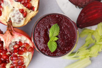 Tasty beetroot smoothie with mint in glass, fresh vegetables and pomegranate on light table, flat lay. Vegan drink