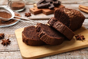 Delicious cut chocolate sponge cake and ingredients on wooden table, closeup