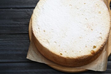Delicious sponge cake with powdered sugar on black wooden table, above view