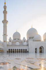 Obraz premium Courtyard of Sheikh Zayed Grand Mosque in Abu Dhabi, UAE with white marble domes, minaret and floral marble flooring at sunset. Islamic art and architecture. Vertical orientation