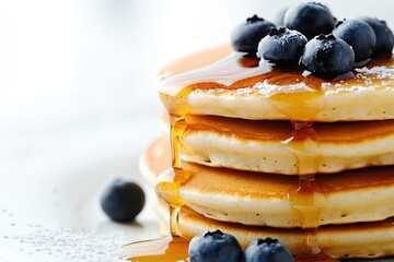 A stack of fluffy pancakes drizzled with maple syrup and topped with fresh blueberries