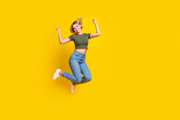 Full size photo of satisfied girl dressed khaki crop top jeans jumping raising arms up win bet isolated on yellow color background