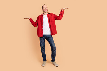 Full length portrait of nice young man show empty space wear red shirt isolated on beige color background