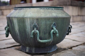 Ancient bronze cauldron with intricate handles on stone pavement.