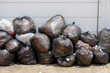Pile of plastic trash bags at the white wall outside the building, wait for the garbage truck
