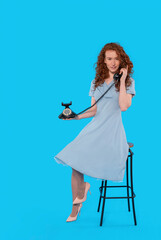 Young Woman in Blue Dress Sits Gracefully With Vintage Phone Against  Bright Backdrop