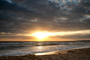 Sunset over sandy beach with waves and dramatic sky