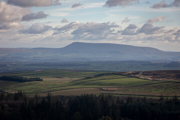 Scenic view of rolling green hills with a distant mountain under a partly cloudy sky in Skipton
