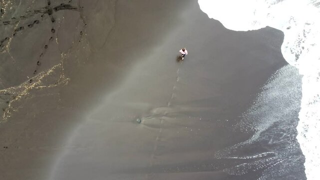 Aerial drone shot of a woman walking through the black sand beach in Acores, Portugal.