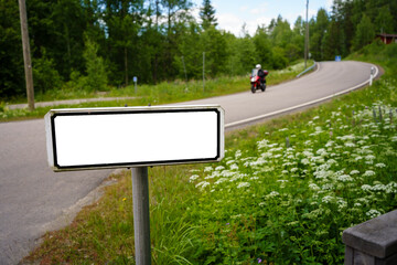 A blank road sign near a winding countryside road