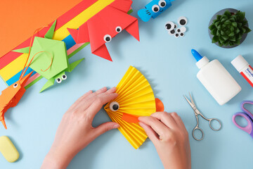 Women's hands make a paper craft of a yellow fish. Around the stationery for paper art scissors,...