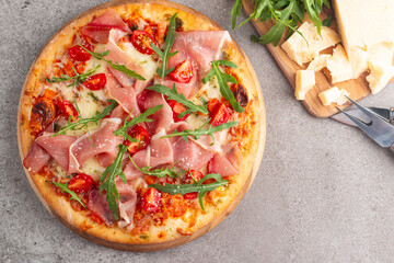 Pizza with prosciutto, ham, arugula, spinach, tomatoes, pesto, cheese and parmesan. Italian cuisine. 