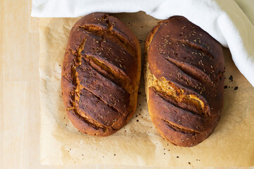 top view of two fresh baked rye bread loafs on a baking paper covered by a white towel