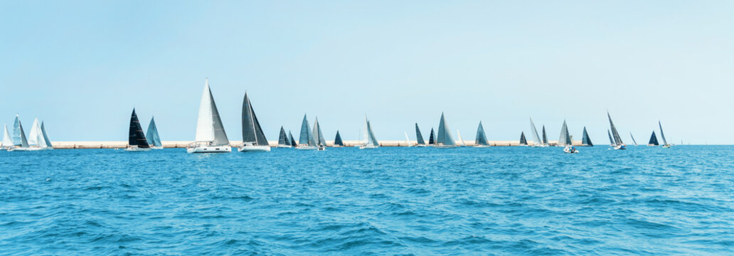 Sailboats near Brindisi under blue cloudless sky. Boats have white and black sails