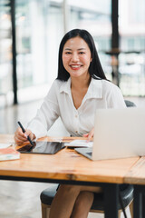 A professional woman smiles while working at desk with laptop and tablet