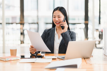 Fototapeta premium A professional woman smiles while talking on phone and reviewing documents