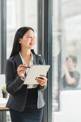 A confident businesswoman smiles while holding tablet in modern office